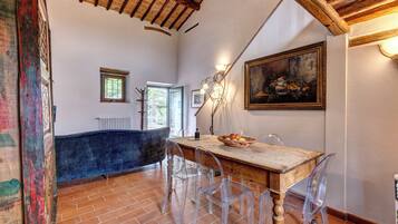 Un comedor con una mesa de madera, sillas transparentes, un cuadro en la pared y un techo rústico.