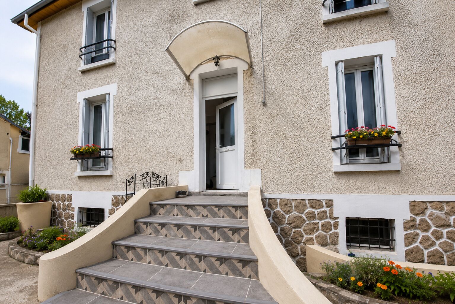 A building with a stone facade, a set of stairs leading to a door, and flower boxes on the windowsills.