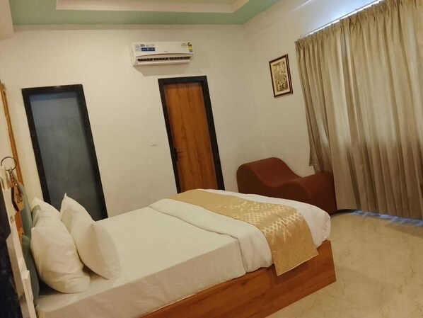 A hotel room with a bed, a chair, an air conditioning unit, a door, and a curtain. - Royal Madhav Niwas (Udaipur)