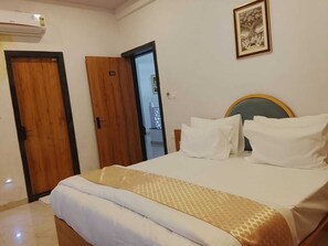 A hotel room with a bed, a wooden door, and a framed picture on the wall. - Royal Madhav Niwas (Udaipur)