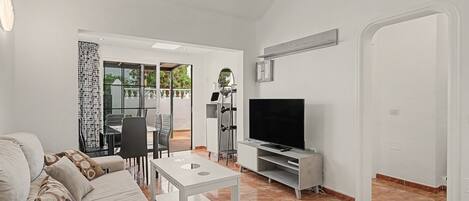 Ein Wohnzimmer mit einer Couch, einem Fernseher, einem kleinen Tisch und einem Essbereich mit Stühlen und Tisch.
