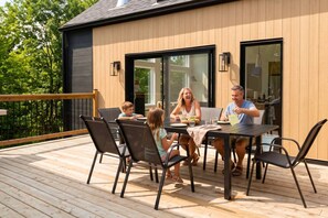 Une famille prend son repas sur une terrasse extérieure, avec une maison moderne en arrière-plan.