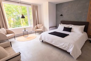 Un dormitorio moderno con una cama grande, una silla, una mesita y vistas a zonas verdes.