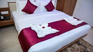 Hotelkamer met een groot bed, wit beddengoed, twee rode kussens, een houten hoofdeinde, een nachtkastje met een telefoon en een kamerkleed met een patroon.