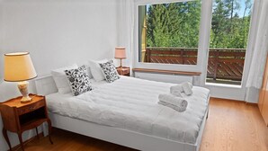 A neatly made bed with white linens, two pillows with black patterns, a bedside lamp, and a window with a view of greenery. - Renovated apartment, large balcony, 10 minutes from the slopes (Crans-Montana)