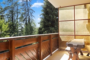 Ein Balkon mit Holzgeländer, einem Steintisch und Blick auf hohe Bäume.