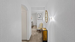 A hallway with a white door, a framed artwork on the wall, a chair, and a table with a decorative box. - Renovated apartment, large balcony, 10 minutes from the slopes (Crans-Montana)