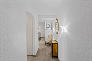 Ein Flur mit einer weißen Tür, einem gerahmten Kunstwerk an der Wand, einem Stuhl und einem Tisch mit einer dekorativen Schachtel.