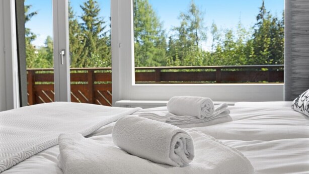 A hotel room with a bed, a window with a view of trees, and a wooden deck outside. - Renovated apartment, large balcony, 10 minutes from the slopes (Crans-Montana)