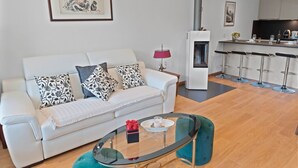 A modern living room with a white sofa, patterned cushions, a glass coffee table, and a teal ottoman. - Renovated apartment, large balcony, 10 minutes from the slopes (Crans-Montana)