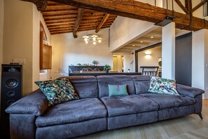 Ein modernes Wohnzimmer mit Ledersofa, Holzbalken und einer Küche im Hintergrund.
