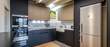 Une cuisine moderne dotée d’appareils électroménagers en acier inoxydable, de meubles de rangement aux couleurs sombres et d’un plan de travail en marbre.