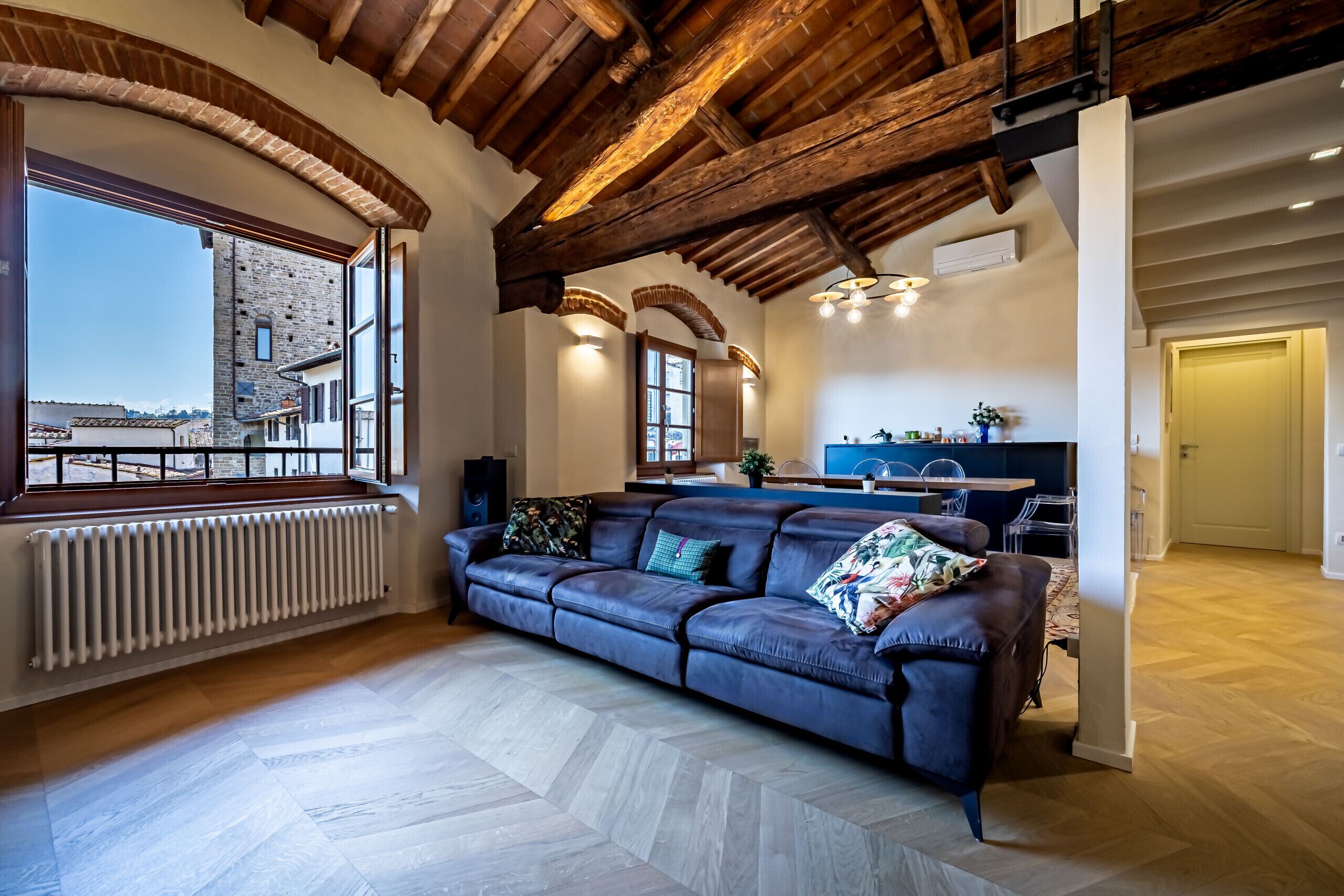 Een moderne woonkamer met een leren bank, een houten plafond en een groot raam met uitzicht op een gebouw.