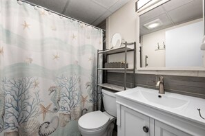 A bathroom with a shower curtain featuring sea-themed designs, a white toilet, a vanity with a mirror and shelves, and a modern faucet. - Two-bed, two-bath, ocean-block condominium ideally located on 44th St (Ocean City)