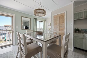 A dining area with a glass-top table, wicker chairs, a hanging light fixture, and a view of the outside. - Two-bed, two-bath, ocean-block condominium ideally located on 44th St (Ocean City)