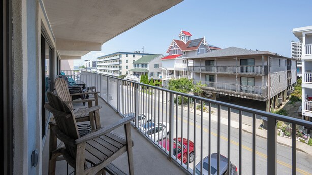 Ein Balkon mit Holzstühlen, Blick auf eine Straße mit Autos und Häuser mit Balkonen.