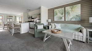 Ein modernes Wohnzimmer mit einer Couch, einem Essbereich mit Stühlen, einer Küche mit Geräten und einem großen Fenster.