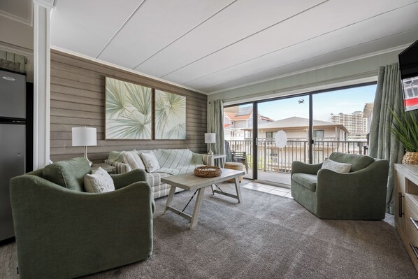 A modern living room with a sofa set, a coffee table, and a dining table. There is a balcony with a view of the city. - Two-bed, two-bath, ocean-block condominium ideally located on 44th St (Ocean City)