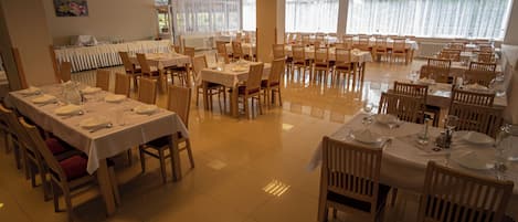 A spacious dining area with multiple tables set for service, large windows providing natural light, and a clean, tiled floor.