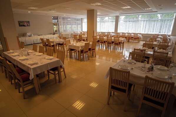 Un comedor amplio con varias mesas dispuestas para el servicio, grandes ventanales que brindan luz natural y un piso de baldosas impecable.