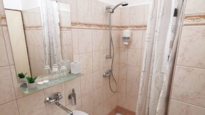 A bathroom with a bathtub, a shower, a glass shelf with toiletries, and a mirror. - Hotel Preveza (Spišská Nová Ves)
