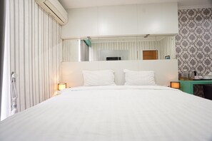 A hotel room with a large bed, a mirror above the bed, a bedside table with a lamp, and a window with curtains. - Oak Damar • Deluxe Comfort Room (Gresik)