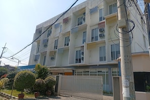 A multi-story building with air conditioning units on each floor, a gated entrance, and a sign indicating a cost of living area.