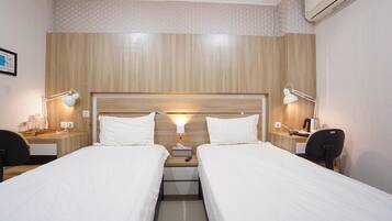 Ein Hotelzimmer mit zwei Einzelbetten, Nachttischen mit Lampen, einem kleinen Schreibtisch und einer Klimaanlage.