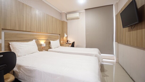 Habitación de hotel con dos camas, un escritorio con silla, un televisor de pantalla plana en la pared y un equipo de aire acondicionado.