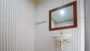 Un baño con pared de baldosas a rayas, espejo con marco de madera y lavamanos blanco.