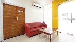 Zona de recepción con un sofá rojo, una puerta de madera con la leyenda 'BUNG TOMO' y un equipo de aire acondicionado.