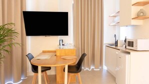 Moderni huone, jossa on ruokapöytä, tuolit, seinälle asennettu taulutelevisio, mikroaaltouuni ja ruukkukasvi.