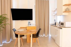 Ein modernes Zimmer mit Esstisch, Stühlen, einem an der Wand montierten Flachbildfernseher, einer Mikrowelle und einer Topfpflanze.