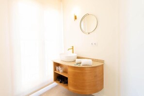 Ein Badezimmer mit einem weißen Waschbecken, einem goldenen Wasserhahn und einem Holztischchen.
