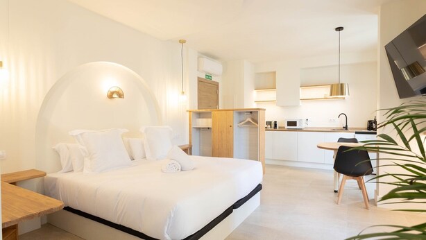 Moderni hotellihuone, jossa on suuri sänky, pieni keittiö ja ruokailutila.