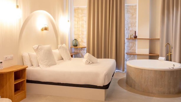 Habitació d'hotel moderna amb un llit gran, una banyera rodona i una taula auxiliar de fusta.