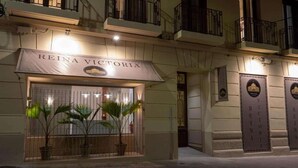 Entrada d'hotel amb un rètol que diu 'REINA VICTORIA' i una entrada reixada amb plantes en testos.