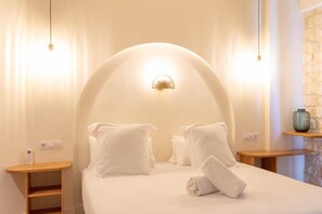Une chambre d’hôtel avec un plafond incurvé, un lit avec du linge de lit blanc, deux tables de chevet et un luminaire fixé au mur.