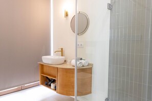 Ein modernes Badezimmer mit einem weißen Waschbecken, einem goldenen Wasserhahn und einem Spiegel darüber.