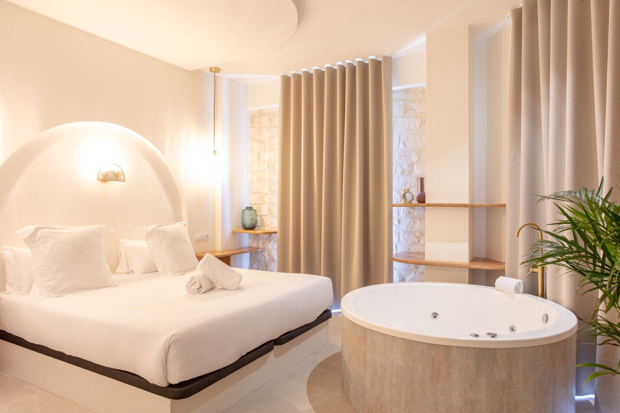 A modern bedroom with a large bed, a round bathtub, and a stone wall.