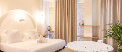A modern bedroom with a large bed, a round bathtub, and a stone wall.