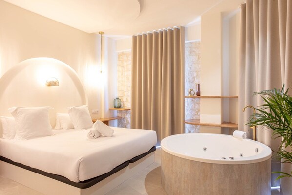 A modern bedroom with a large bed, a round bathtub, and a stone wall.
