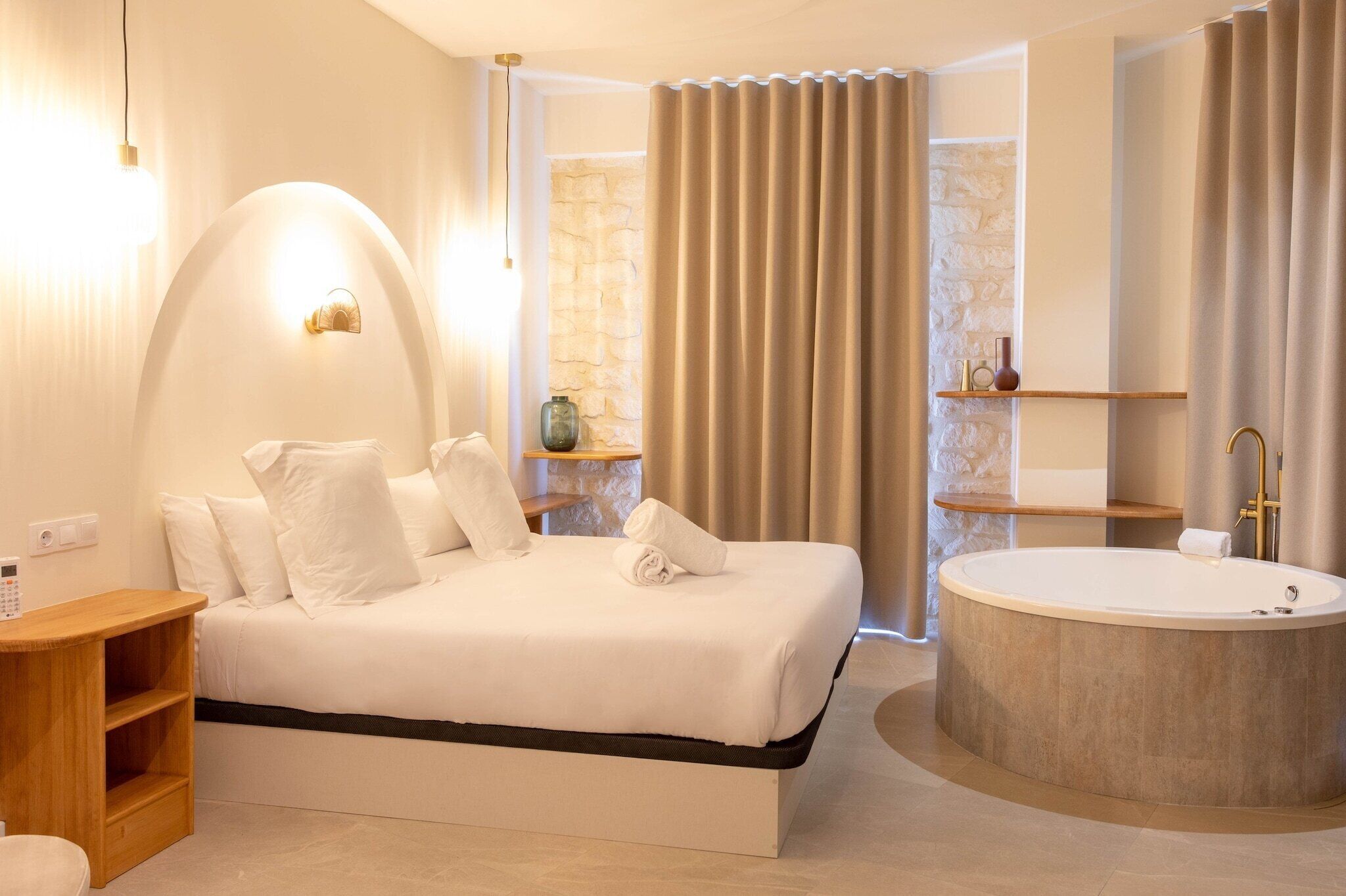 A modern bedroom with a large bed, a round bathtub, and a wooden bedside table.