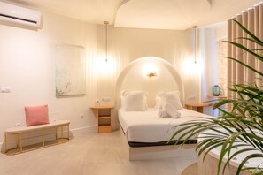 Ein modernes Schlafzimmer mit einem gewölbten Kopfteil, einer Bank mit rosa Kissen, Nachttischen und einer großen Kübelpflanze.