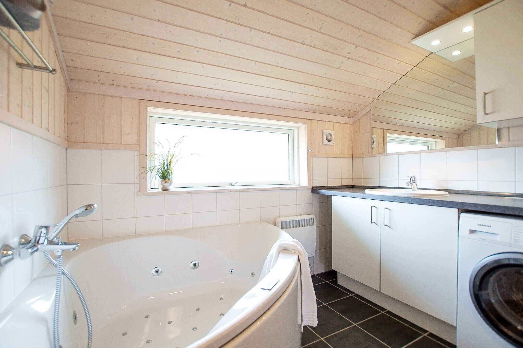 Un bagno moderno con una vasca, un lavandino, una lavatrice e una finestra con una pianta.