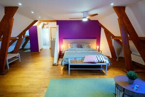 A bedroom with a sloped ceiling, wooden beams, a bed with floral bedding, a bedside table, and a small potted plant. - Chambres d'Hôtes La Bonne Voie (Lembras)