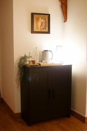 Un meuble de couleur sombre, doté de deux portes, avec un tableau encadré accroché au mur au-dessus, et une plante placée sur le côté gauche.