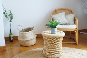 Uma cadeira de vime com uma almofada, um banquinho trançado com uma planta e uma cesta de vime.