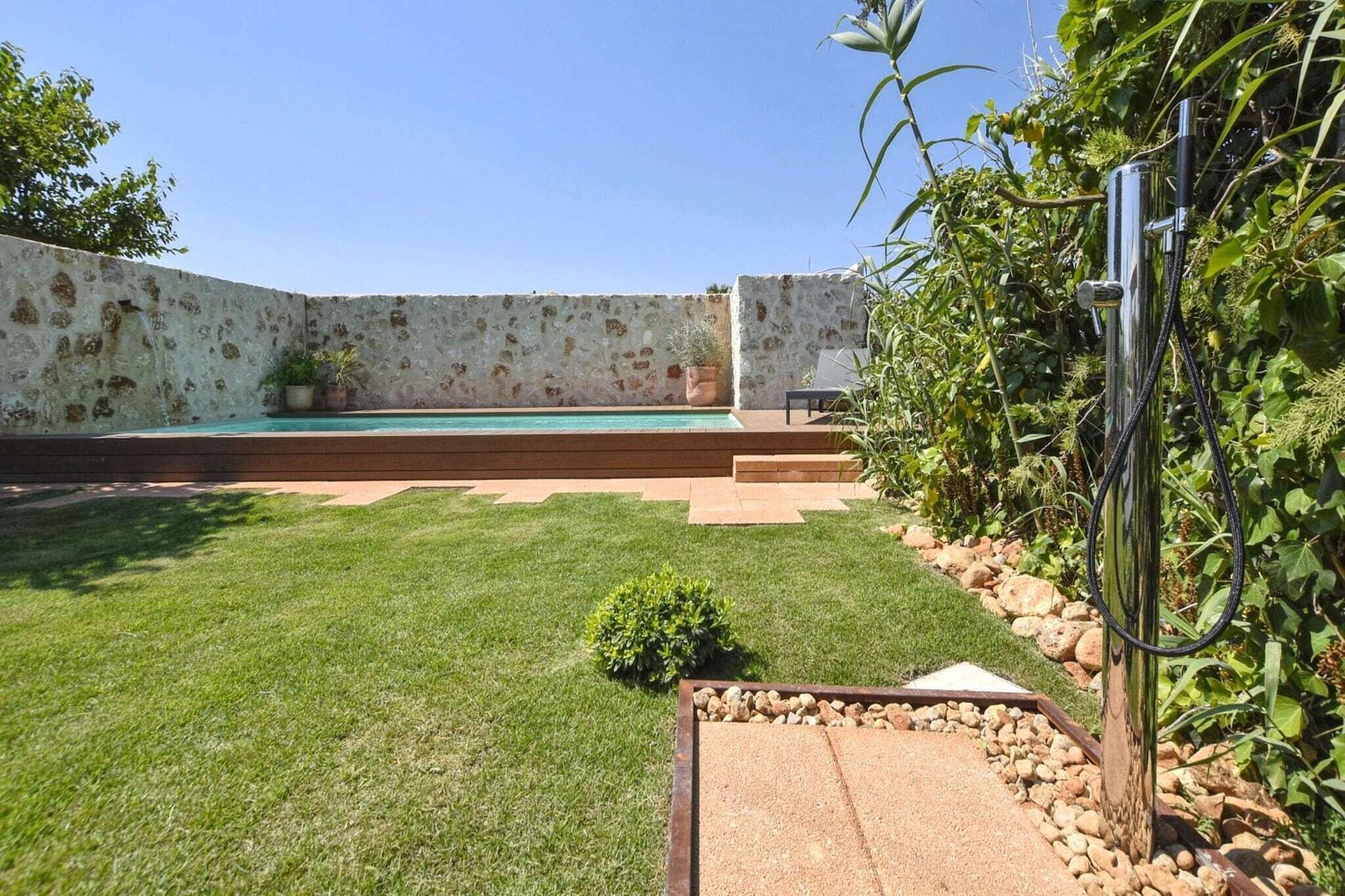 A backyard with a swimming pool, a stone wall, and a garden area with plants and a small bush.