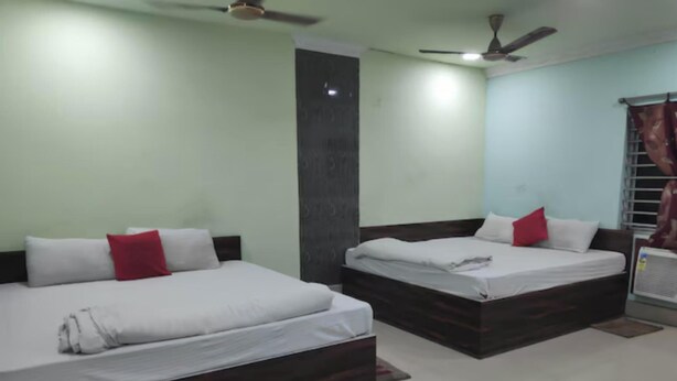 A hotel room with two beds, each with white linens and red pillows, a ceiling fan, and a window with curtains. - Hotel Shakti (Cuttack)